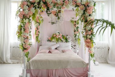 Balayı Süiti gölgelik yatak, boş alan. Çiçekler ve yastıklar üzerine lüks ahşap gölgelik yatak. Kadın yatak odasında pembe ve beyaz renkler, kopya alanı. Şık yatak odasında büyük rahat yatak