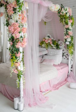 Balayı Süiti gölgelik yatak, boş alan. Çiçekler ve yastıklar üzerine lüks ahşap gölgelik yatak. Kadın yatak odasında pembe ve beyaz renkler, kopya alanı. Şık yatak odasında büyük rahat yatak