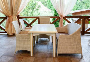 Rattan hasır koltuk ve yaz bahçe terası açık boş alan masada boş kafe. Masa ve sandalyeler boş kafede. Hasır mobilya rattan sandalye ve koltuk terasta  