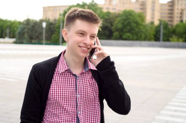 Neşeli genç adam ekose gömlek ve şehirde yürüyüş ve cep telefonu açık havada üzerinde söz ceket boş alan. Mobil akıllı telefon ile öğrenci