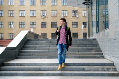 Genç moda yakışıklı ekose gömlek, kot pantolon ve ceket tam vücut uzunluğu, kentin açık havada, merdivenlerde yürüyen sırt çantası ile portresi boş alan