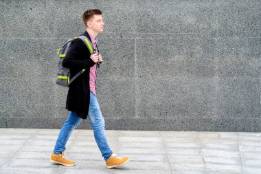 Ekose gömlek ve boş alan açık havada, şehirde yürüyüş sırt çantası ile kot şık genç adam portresi. Taş duvara yakın öğrenci gider