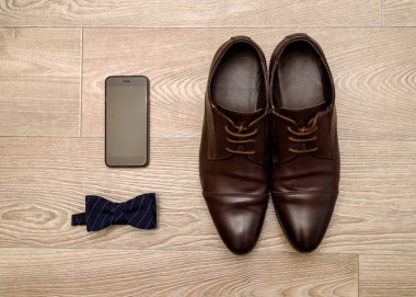 Kahverengi deri ayakkabı Erkek, mavi papyon ve ahşap arka plan, boş alan cep telefonu kapatın. Modern insan aksesuarları. Düğün detayları. Damat aksesuarları. Erkek Ayakkabı ve papyon ile rahat kıyafetler 