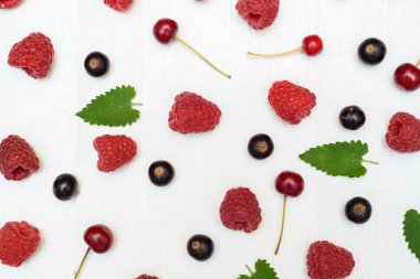 Üstten görünüm tatlı taze organik ahududu, blackcurrants, kiraz ve beyaz ahşap zemin üzerine yeşil yaprakları. Yaz ve sağlıklı gıda kavramı, boş alan. Doğal arka plan 