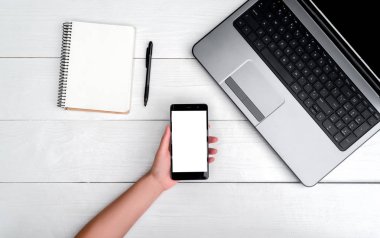 Üstten görünüm açık dizüstü bilgisayar, cep telefonu kızın elinde beyaz ahşap masa ve kalem, boş alan ile boş boş günlüğü. Hareket eden telefon ile boş beyaz ekran, kopya alanı 