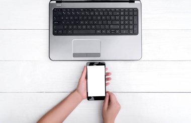 Üstten görünüm ile beyaz tahta masada boş dizüstü bilgisayar ve kızın elleri ile cep telefonu, boş alan açın. Cep telefonu ile beyaz perde, kopya alanı 