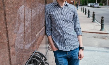 Casual yakışıklı genç ekose gömlek ve şehir açık havada, taş duvarının yakınında ayakta kot boş alan