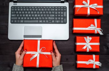 Ahşap masa, kopya alanı üzerinde üstten görünüm açık dizüstü bilgisayar, kırmızı hediye kutuları. Düz yatıyordu. Online alışveriş, satış. Elinde mevcut tutan kadın. Sevgililer günü, 8 Mart (kadınlar günü), anneler günü