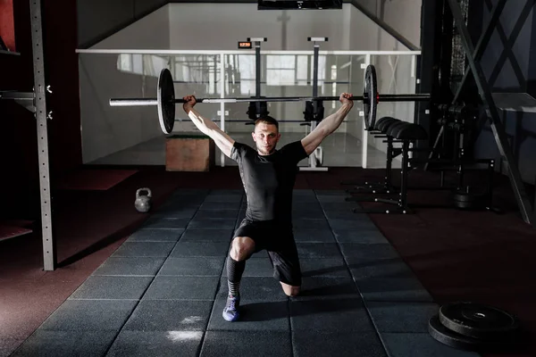 Fit young bearded athlete lifting the barbell in gym. Gym training. Full body length portrait