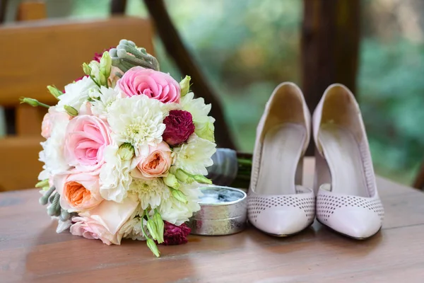 Fresh wedding bouquet near  box with rings and bride shoes in blur on wooden background closeup. Wedding details outdoor. Bouquet and beige bridal shoes. Wedding morning preparation