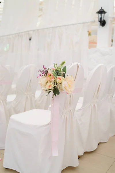 Beautiful flower arrangement on white wedding chairs on each side of archway, selective focus. Empty chairs with white cloth for guests on wedding ceremony, free space