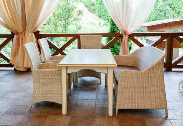 Empty cafe with rattan wicker armchairs and table on summer garden terrace outdoor, free space. Table and chairs in empty cafe. Wicker furniture rattan chairs and sofa on terrace