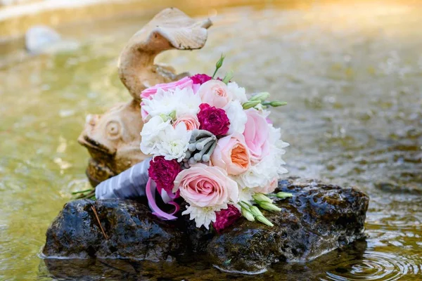 Close up of beautiful fresh wedding bouquet of pink and white roses on stone in water  near fish in fountain, free space. Wedding details outdoor with copy space