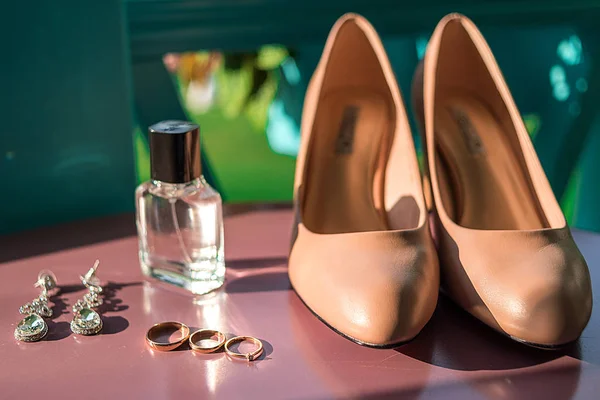 Wedding accessories, selective focus. Bridal shoes, jewelry, perfume bottle, three wedding and engagement rings. Wedding details outdoors. Wedding morning concept