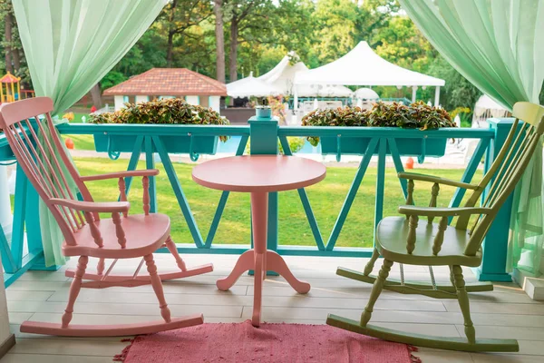 Pink and green wooden rocking chairs and table on porch or balcony. Two relaxing armchairs on porch of luxury hotel. Empty cafe with rocking chairs and table on summer  terrace outdoor, free space
