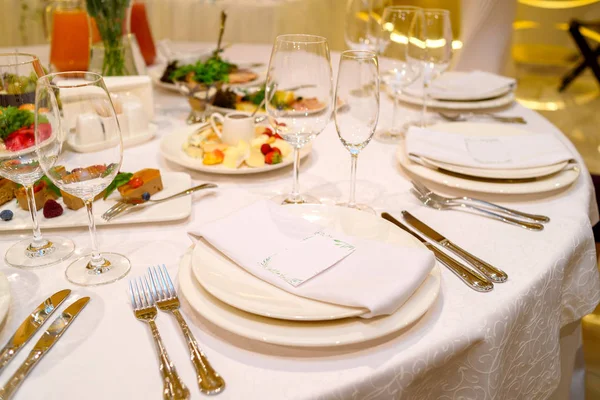 Dinner place setting with blank guest card on white table napkin at wedding reception, copy space for text. Table setting with dishes, glasses and cutlery. Wedding banquet, place card