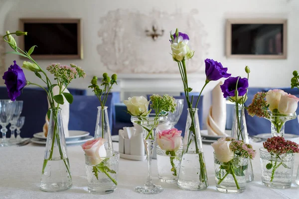 美丽的鲜花在桌子上的婚礼 自由的空间 婚礼桌上装饰 餐厅餐桌上的玻璃花瓶中的粉红色玫瑰和紫色的乌斯托马花束 — 图库照片