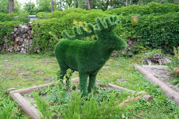 Figure of deer made of green lawn grass in the park, free space. Green grass covered topiary deer, landscape design. Grass figure of deer, topiary figure