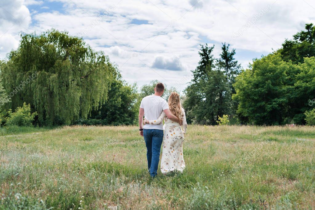 Couple in love embracing and walking outdoors near the forest, back view. Free space