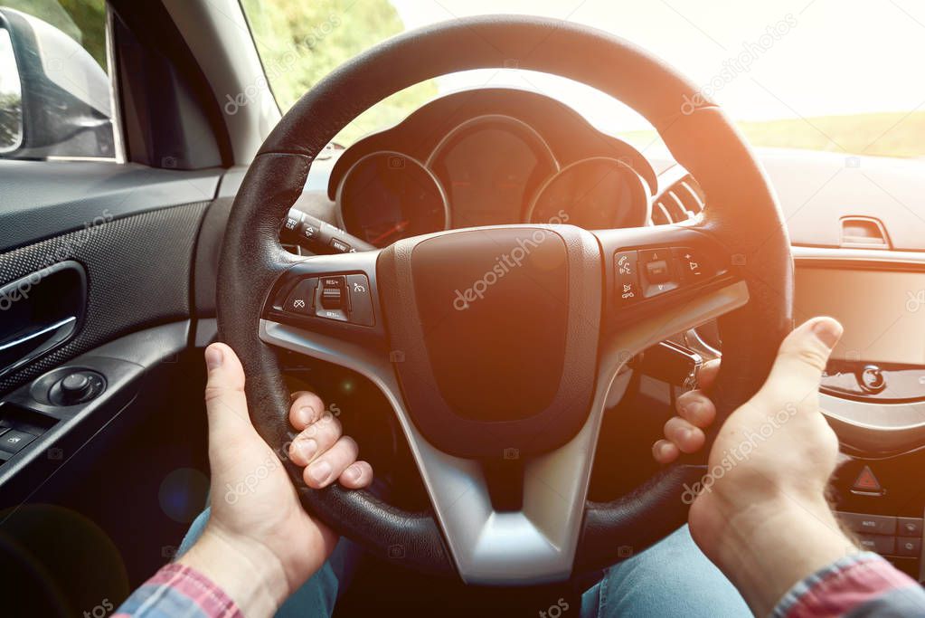 Close up of steering wheel in male driver hands, toned. Man's hands holding steering wheel inside car