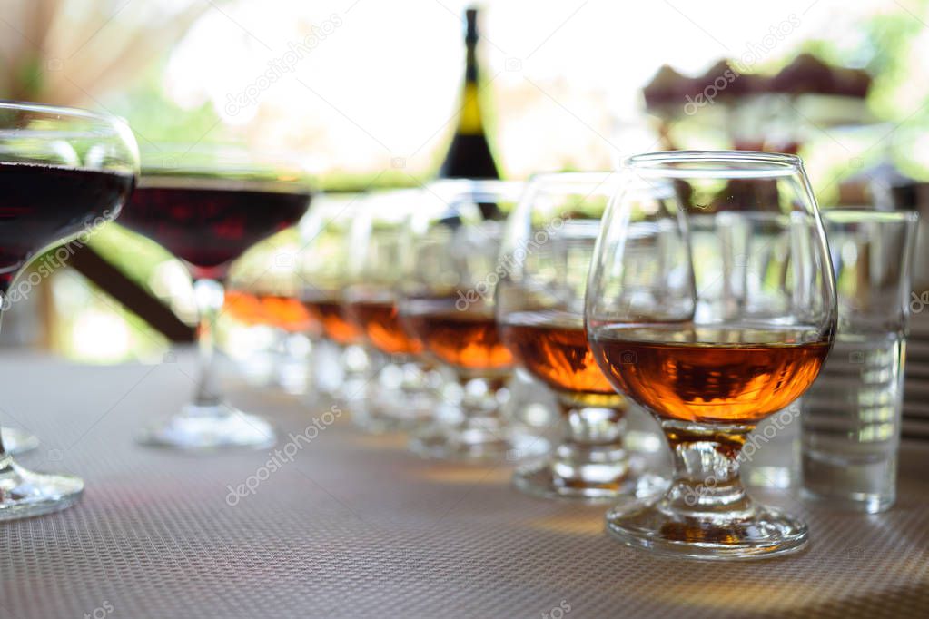 Row of glasses with whiskey or cognac on the table, free space. Strong alcohol in bar or restaurant. Transparent glasses with alcoholic drink