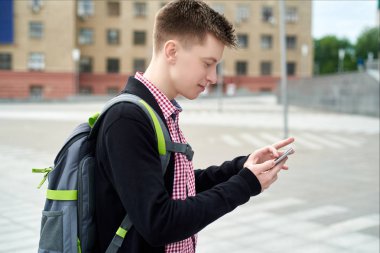 Şehirde yürüyüş ve mobil akıllı telefon açık havada kullanma sırt çantası ile ekose gömlekli şık genç adam. Öğrenci ile smartphone, boş alan. Seyahat kavramı 