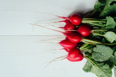 Beyaz ahşap arka planda, kopya alanı üst ve yeşil yapraklarla taze bahçe turp demet. Taze hasat kırmızı turp. Sebze arka plan. Üstten görünüm, düz yatıyordu