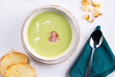 Yeşil bezelye krem çorbası domuz pastırması ve beyaz tahta masada croutons kasede krema ile. Hafif yaz yeşil bezelye çorbası ekmek tost kase. Üstten görünüm, düz yatıyordu