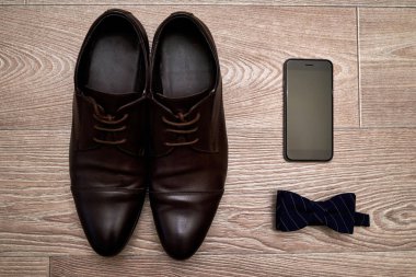 Kahverengi deri erkek ayakkabı, mavi papyon ve ahşap arka plan, boş alan cep telefonu kapatın. Modern insan aksesuarları. Düğün detayları. Damat aksesuarları. Erkek Ayakkabı ve papyon ile rahat kıyafetler 