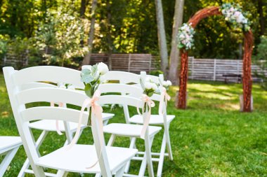 Kemer outroods her tarafında düğün sandalyeye pembe kurdele beyaz taze çiçeklerle; kopya alanı. Konuklar bahçe düğün olarak yeşil çim üzerinde için ahşap sandalye