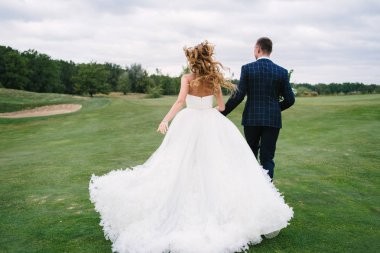 Tam uzunlukta vücut portresi Genç gelin ve damat görünüm golf sahası, geri yeşil çimenlerin üzerinde çalışan. Mutlu evlilik çift golf sahası ile yürüyüş