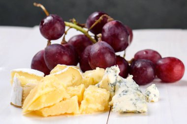 Lezzetli peynir ve üzüm yumuşak Plaque beyaz tahta masada. Camembert peyniri, mavi peynir, yakın. Beyaz arka plan üzerinde peynir parçası 