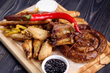 Karışık taze ızgara et ve sosis biber, patates kızartması ve ahşap kesme tahtası üzerinde sos ile. Çeşitli et yemekten yaz barbekü. sağlıklı sebze ile. Lezzetli Mangalda pirzola