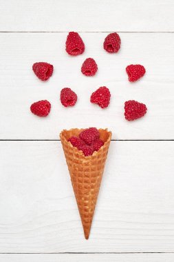 Olgun tatlı ahududu dondurma waffle koni, kopya alanı. Beyaz ahşap zemin, boş alan üzerine taze çilek. Yaz ve sağlıklı gıda kavramı. Üstten görünüm, düz yatıyordu. Çilek arka plan. Ahududu patlama