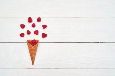 Olgun tatlı ahududu dondurma waffle koni, kopya alanı. Beyaz ahşap zemin, boş alan üzerine taze çilek. Yaz ve sağlıklı gıda kavramı. Üstten görünüm, düz yatıyordu. Çilek arka plan. Ahududu patlama