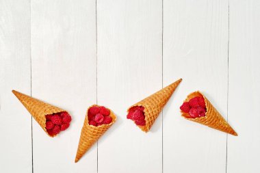 Olgun tatlı ahududu dondurma waffle koni, kopya alanı. Beyaz ahşap zemin, boş alan üzerine taze çilek. Yaz ve sağlıklı gıda kavramı. Üstten görünüm, düz yatıyordu. Çilek arka plan