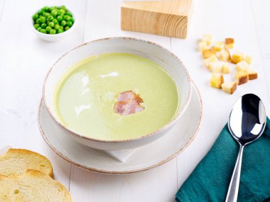 Yeşil bezelye krem çorbası domuz pastırması ve beyaz tahta masada croutons kasede krema ile. Hafif yaz yeşil bezelye çorbası ekmek tost kase