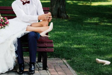 Bankta oturan ve kopya alanı park açık havada, rahatlatıcı bir düğün çift. Damat gelini için ayak masajı yapıyor. Kocası onun karısı ayak masaj. Yüksek topuklu giyen ağrı