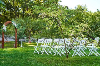 Düğün için çiçek ve açık havada, kemerli her tarafında beyaz sandalye süslenmiş düğün kemer kopya alanı yerleştirin. Konuklar bahçede yeşil çimenlerin üzerinde için boş ahşap sandalye