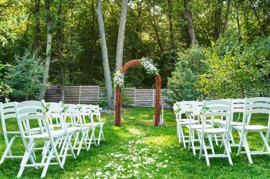 Düğün için çiçek ve açık havada, kemerli her tarafında beyaz sandalye süslenmiş düğün kemer kopya alanı yerleştirin. Konuklar bahçede yeşil çimenlerin üzerinde için boş ahşap sandalye