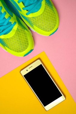 Çift spor ayakkabı ve renkli arka plan üzerinde Mobil cep telefonu. Pembe ve sarı arka plan, kopya alanı üzerinde yeni spor ayakkabıları. Genel gider atış koşu ayakkabıları ve smartphone. Üstten görünüm, düz yatıyordu