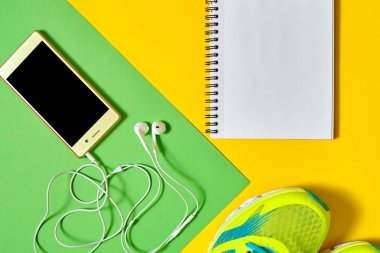 Renkli arka plan, kopya alanı üzerinde üstten görünüm spor ayakkabı, boş boş defter ve kulaklık ile mobil cep telefonu. Düz yatıyordu. Spor, fitness kavramı, sağlıklı yaşam tarzı