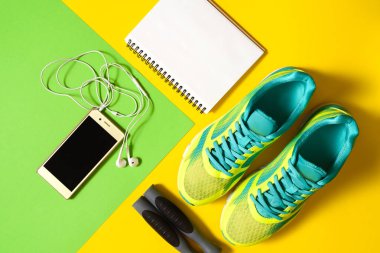 Ayakkabı, renkli arka plan üzerinde atlama ipi, boş defter ve kulaklık ile mobil cep telefonu ile spor malzemeleri. Üstten görünüm, düz yatıyordu. Spor, fitness kavramı, sağlıklı yaşam tarzı