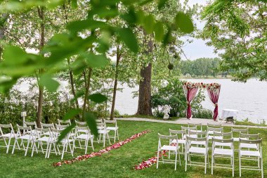 Düğün töreni için kumaş, çiçek ve açık havada, kemerli her tarafında beyaz sandalye dekore düğün kemer kopya alanı yerleştirin. Yeşil çimenlerin üzerinde Konuklar için boş ahşap sandalyeler. Düğün Kur