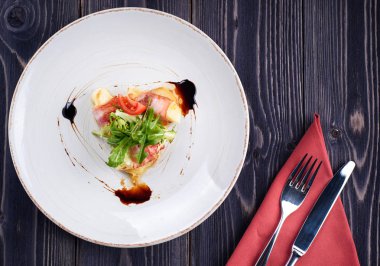 Beyaz tabak ve çatal bıçak takımı peçete, kopya alanı üzerinde lezzetli ızgara domuz pastırması rulo peynir, otlar ve sos ile. Fırında peynirli pastırma sarılmış. Üstten görünüm, düz yatıyordu. Yukarıdan görüntülemek