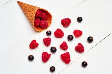 Üstten görünüm tatlı taze organik ahududu ve dondurma waffle koni siyah kuş üzümü. Taze çilek koni Beyaz ahşap zemin üzerinde. Yaz ve sağlıklı gıda kavramı. Çilek arka plan