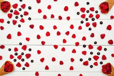 Üstten görünüm tatlı taze organik ahududu ve gözleme koni boş boş alan ile siyah kuş üzümü. Taze çilek koni Beyaz ahşap zemin üzerinde. Yaz ve sağlıklı gıda kavramı 