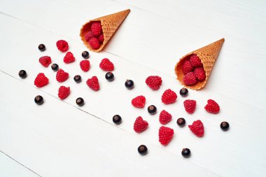 Üstten görünüm tatlı taze organik ahududu ve gözleme koni boş boş alan ile siyah kuş üzümü. Taze çilek koni Beyaz ahşap zemin üzerinde. Yaz ve sağlıklı gıda kavramı 