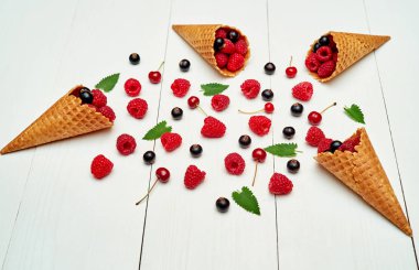 Üstten görünüm tatlı taze organik ahududu, siyah kuş üzümü ve kiraz gözleme koni boş boş alana sahip. Taze çilek koni Beyaz ahşap zemin üzerinde. Yaz ve sağlıklı gıda kavramı 