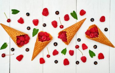 Üstten görünüm tatlı taze organik ahududu, siyah kuş üzümü ve kiraz gözleme koni boş boş alana sahip. Taze çilek koni Beyaz ahşap zemin üzerinde. Yaz ve sağlıklı gıda kavramı 